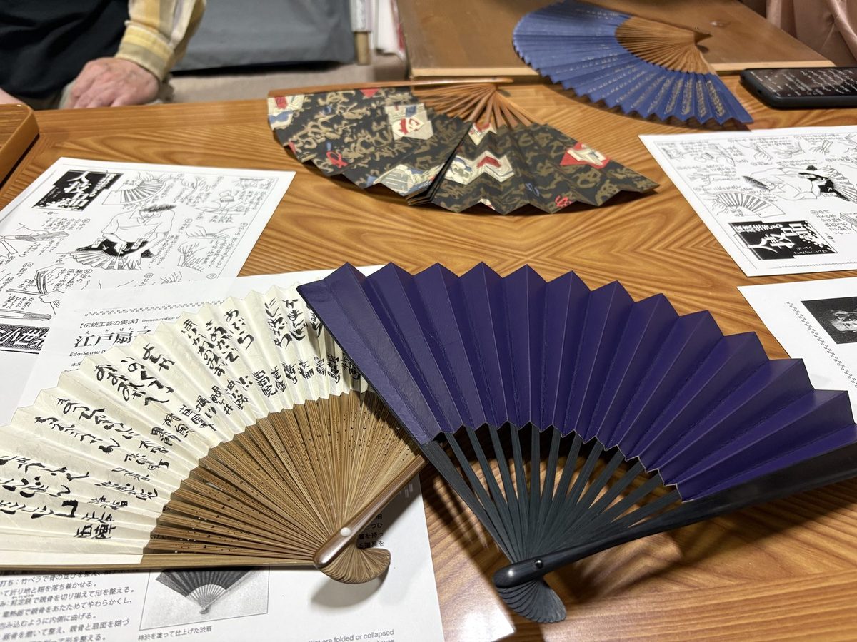 工房の机に広げられた扇子。書の入った扇、藍の扇、柄の扇が並ぶ
